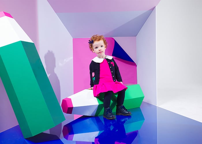 Petite fille dans une tenue d’école assise sur un crayon de papier de décor.